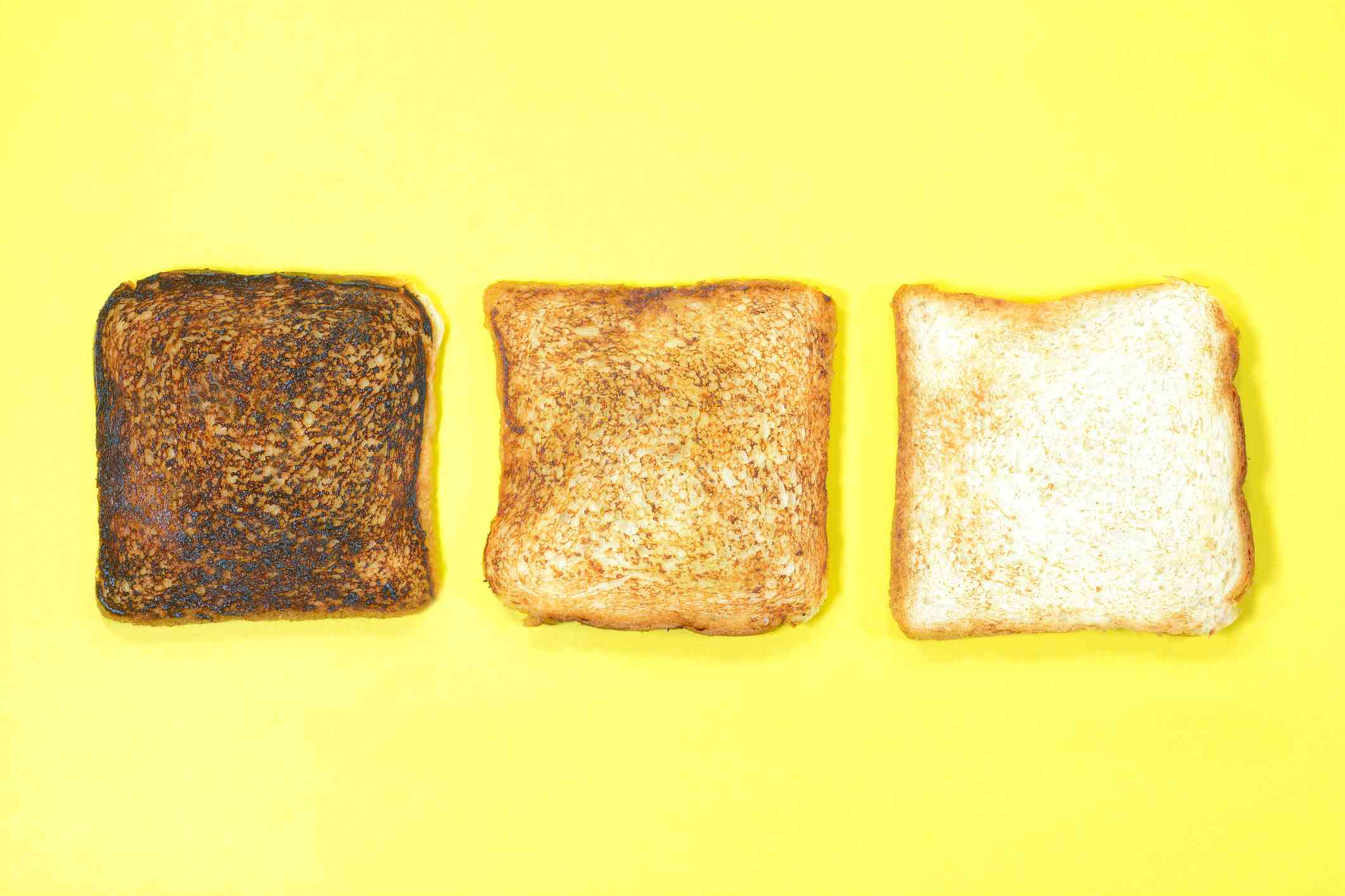 Schlecht verbrannte, richtig geröstete und normale Brotscheibe auf gelbem Hintergrund.