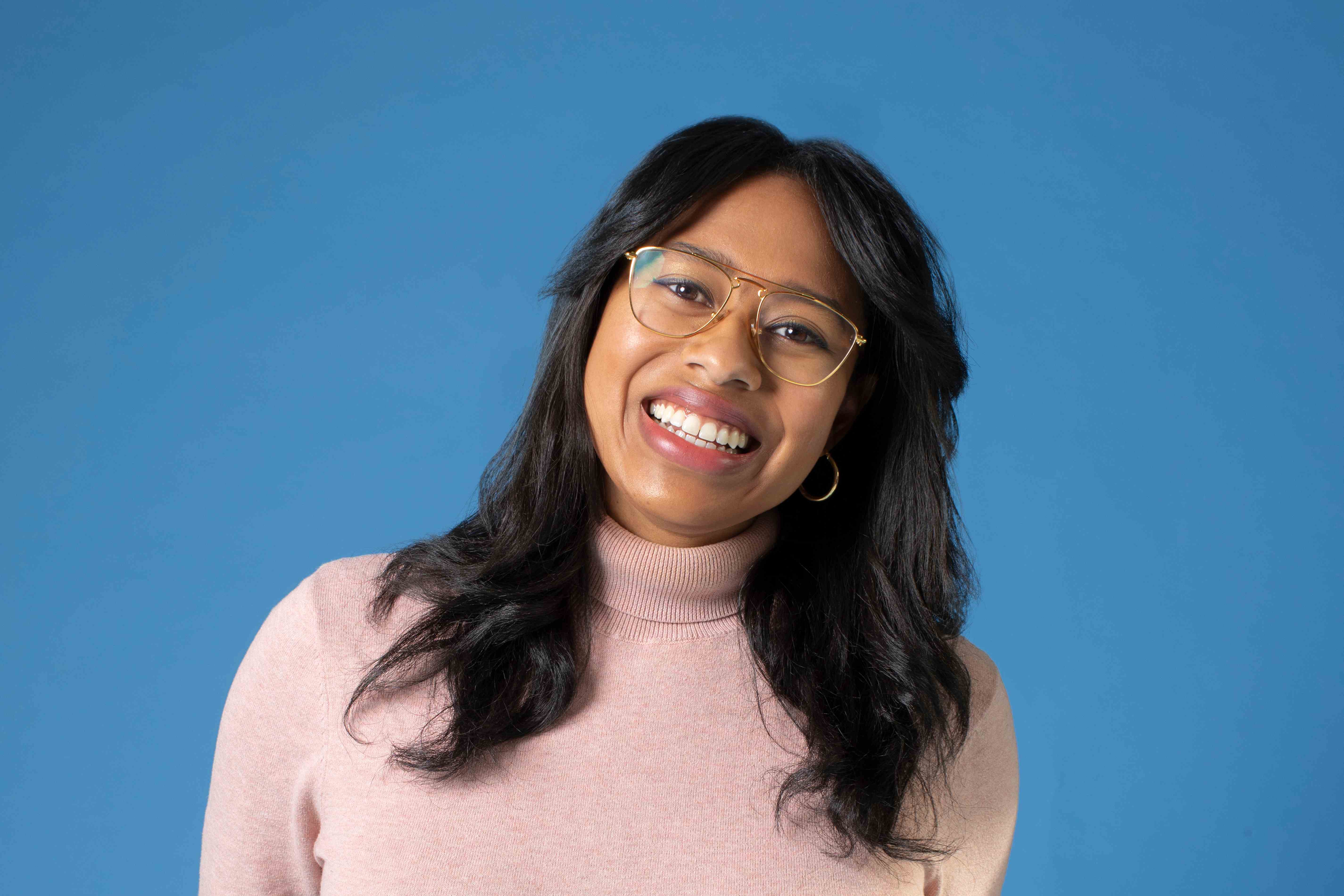 Pilar Johnson lächelt mit Brille und rosa Rollkragenpullover in die Kamera