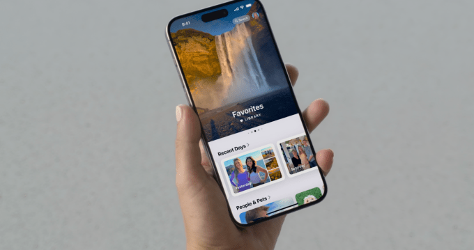 Die Apple Photos-App wird für iOS 18 überarbeitet. Hand hält ein iPhone, auf dem die Fotos-App angezeigt wird